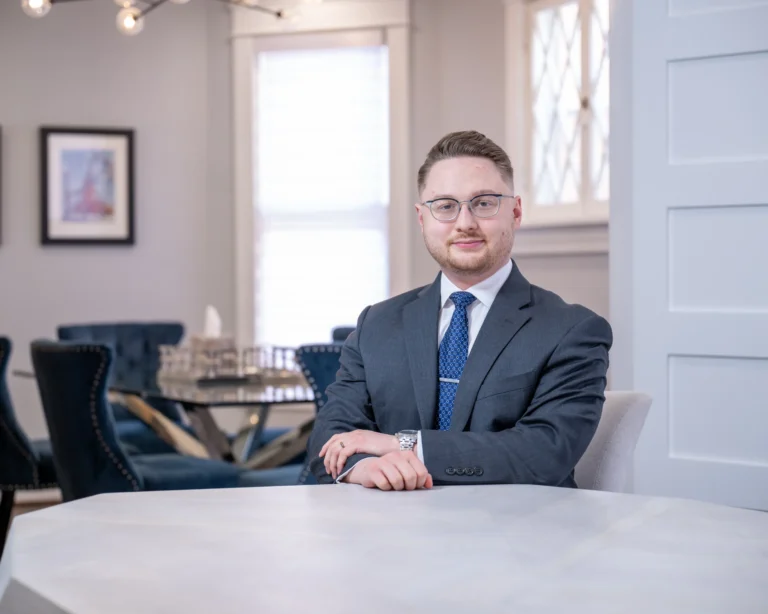 Professional man with glasses and suit seated at a marble table in an office setting.