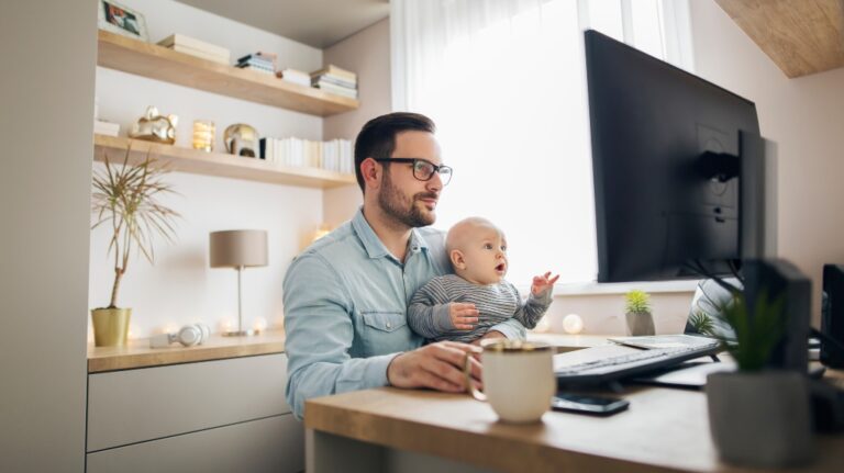 man holding a small child in his arms and working on a computer