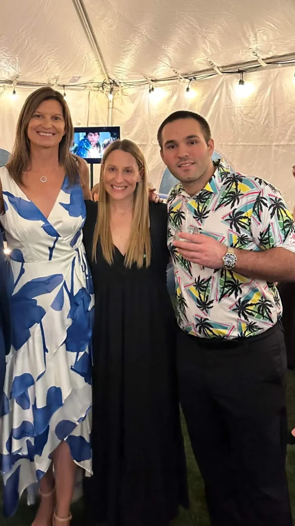 Three people stand together in a tent during an annual party, smiling and enjoying the festive atmosphere.