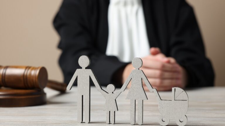 Judge with gavel sitting at white wooden table, focus on figure of parents and children