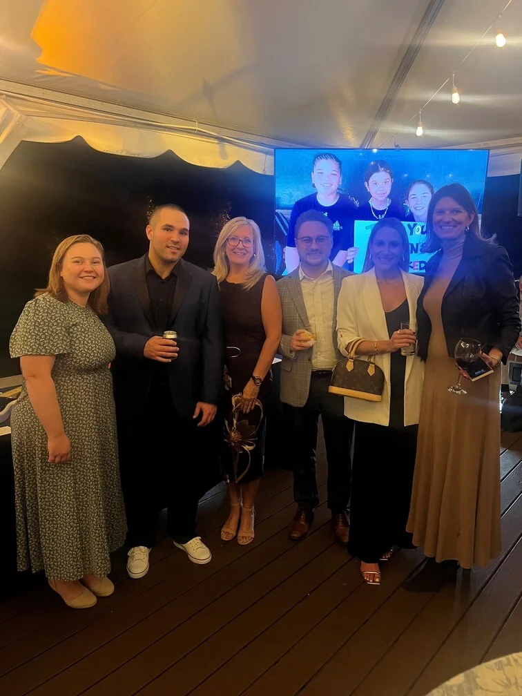 A group of people standing together, facing a large screen displaying information or visuals.