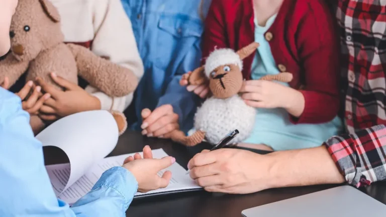 Adults and children sitting at a table with stuffed animals and signing documents.