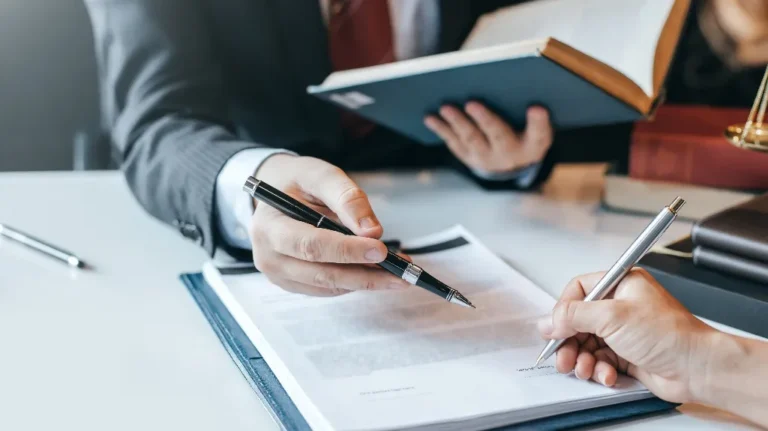 Two professionals in suits reviewing and signing a legal document at a desk.