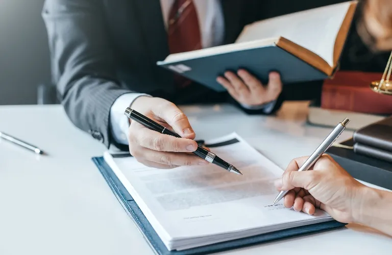Two professionals in business attire reviewing and signing a document at a desk.