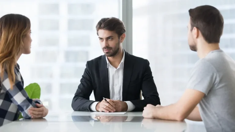 Professional man in black suit conducting a serious discussion with two casually dressed individuals.