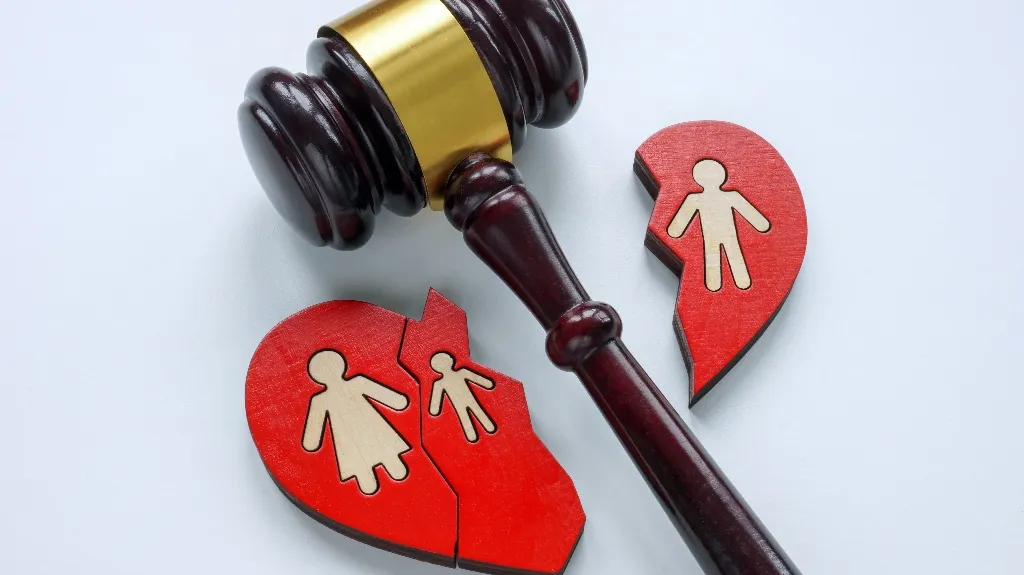 Wooden judge's gavel next to broken red heart-shaped puzzle pieces depicting family figures.