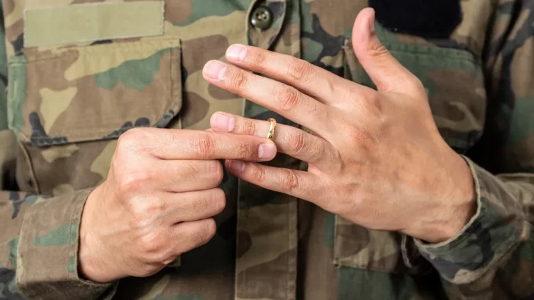 Close-up of a person in camouflage uniform removing a gold wedding ring from their finger.