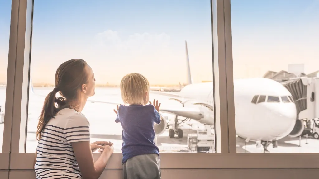 Woman and child looking through airport window at a parked white airplane outside.