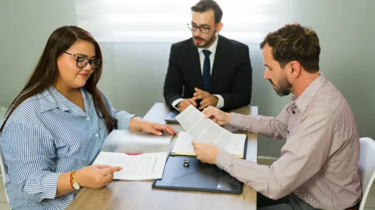 Three professionals reviewing documents at a conference table in a well-lit office.