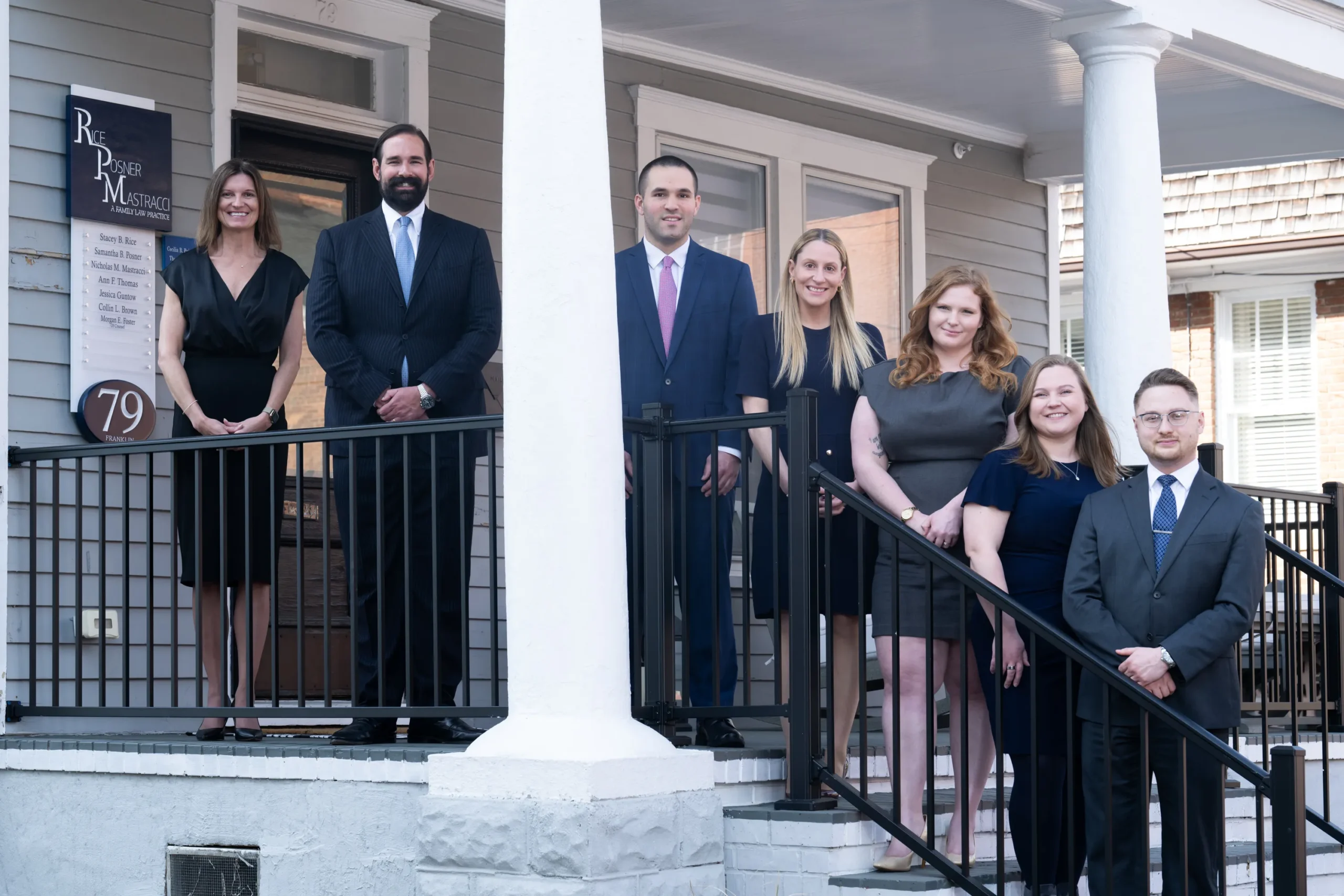 Group of six professionally dressed individuals standing on the porch of a family law practice building.