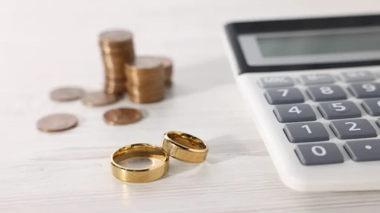 Two gold wedding rings, stacked coins, and a calculator on a white surface.