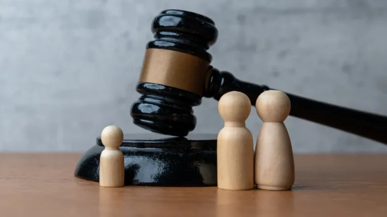 Black wooden judge's gavel beside three varying-sized beige wooden figurines on a wooden surface.