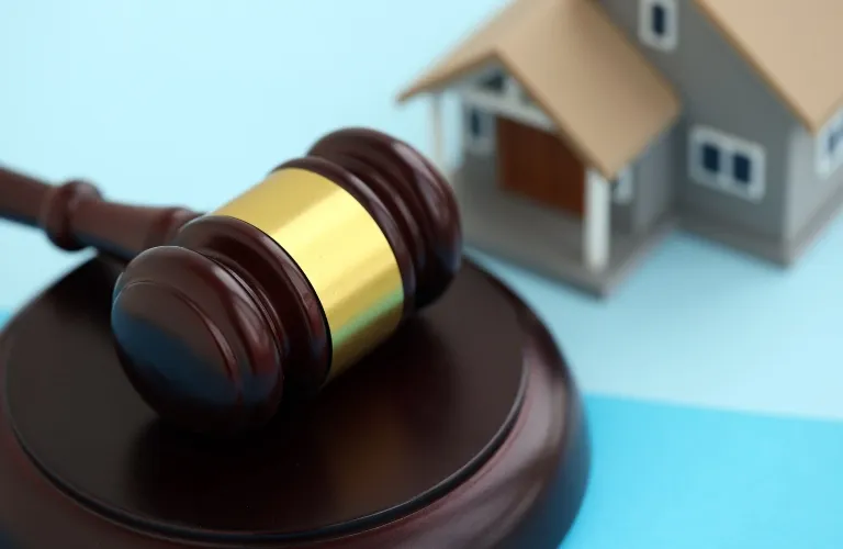 Close-up of a wooden judge's gavel with brass band beside a small model house.