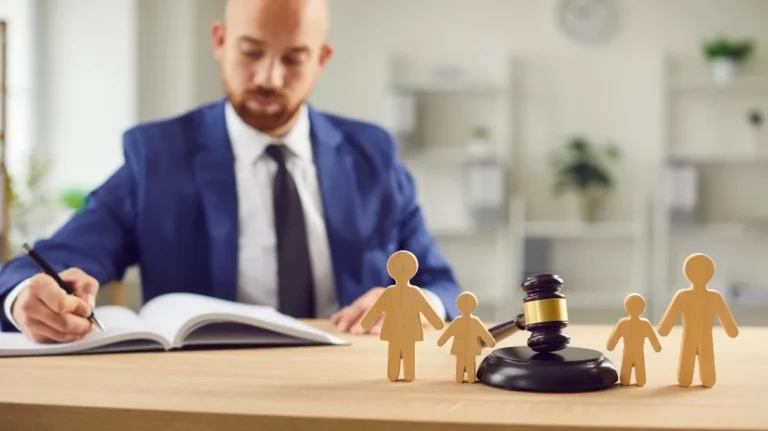 Professional man in blue suit writing, with wooden family figures and judge gavel on desk.