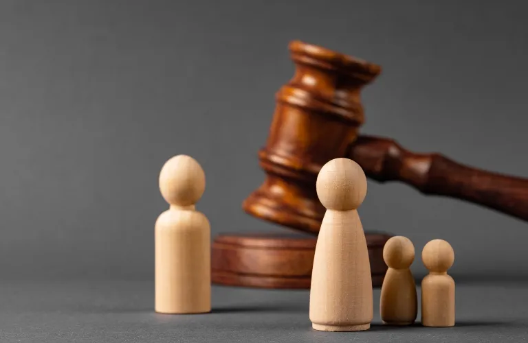 Wooden figurines of varying sizes positioned before a judge's wooden gavel on gray background.