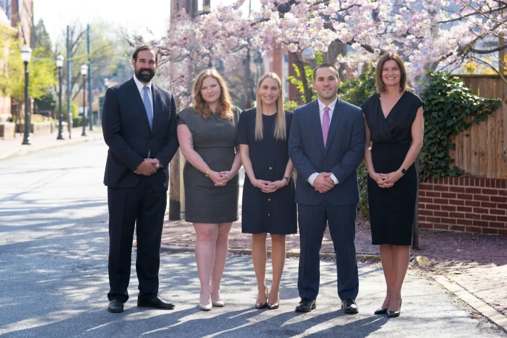 Five professionally dressed individuals standing outdoors on a street with blooming cherry blossom trees.