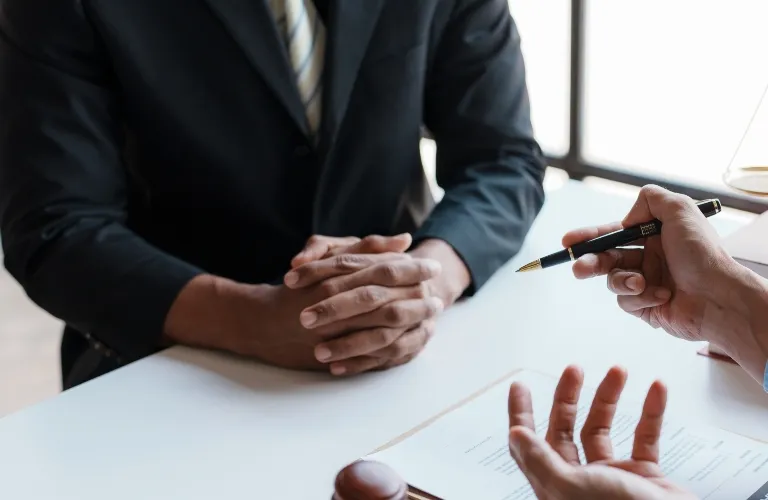 Two individuals in formal attire engaged in a discussion over documents at a white table.