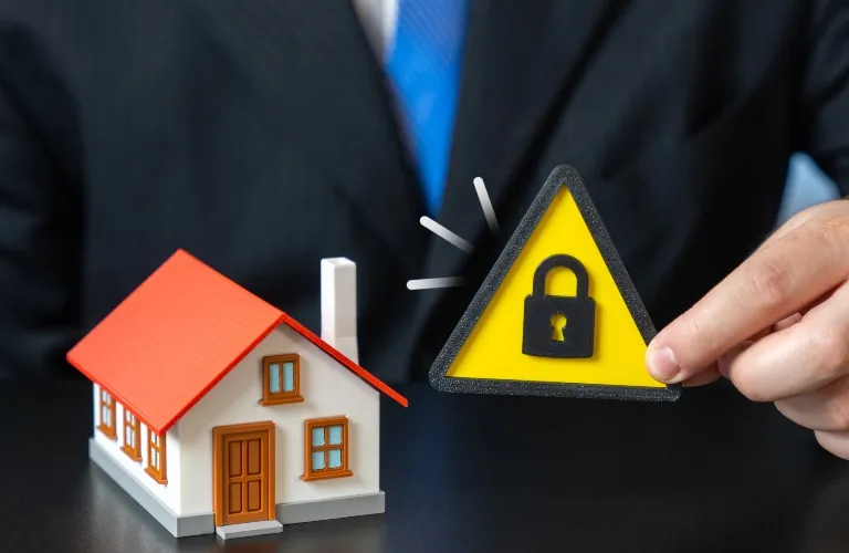 Person in suit holding yellow warning sign with lock symbol next to small house model.