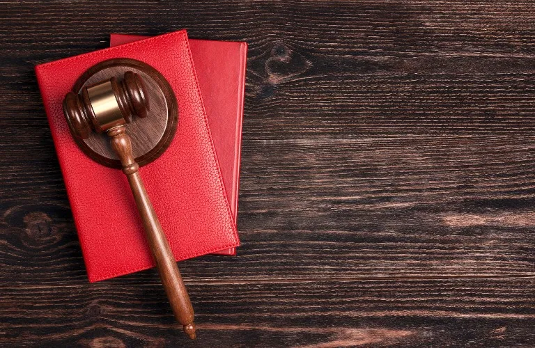 Wooden judge's gavel resting on two stacked red leather-bound books on dark wood.