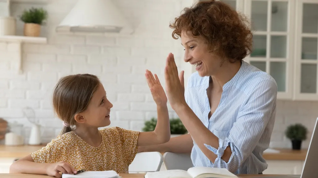 Woman and young girl smiling and giving a high-five in a bright kitchen setting.