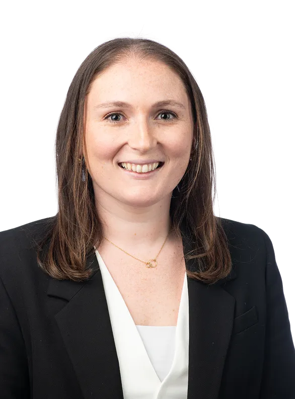 Professional headshot of a smiling woman with shoulder-length brown hair, wearing a black blazer, white blouse, and gold necklace.